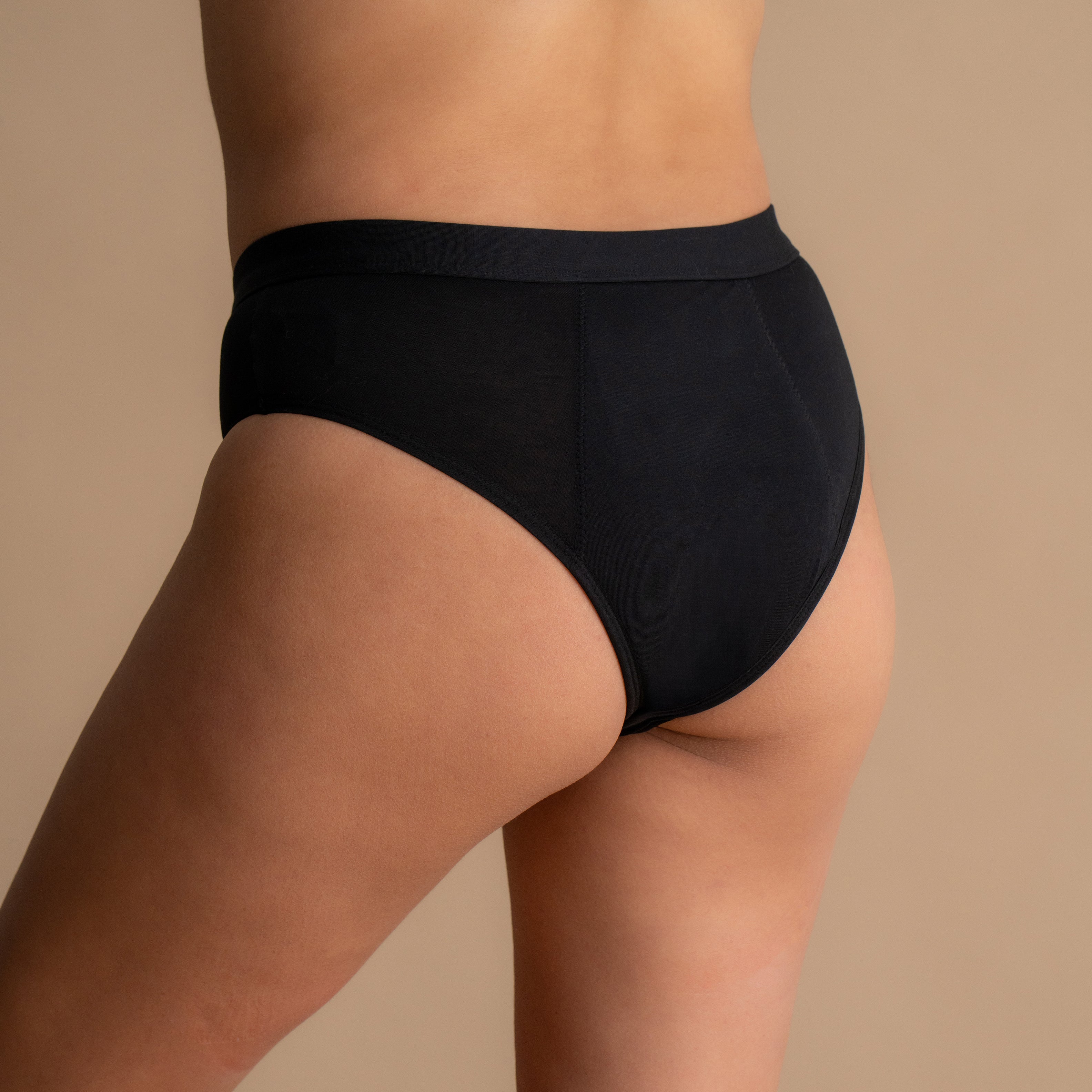 Back view of the model wearing the Leakproof Everyday Bamboo Bikini in black, highlighting the smooth waistband and the comfortable fit. The model stands naturally, showing the bikini's coverage and seamless design.