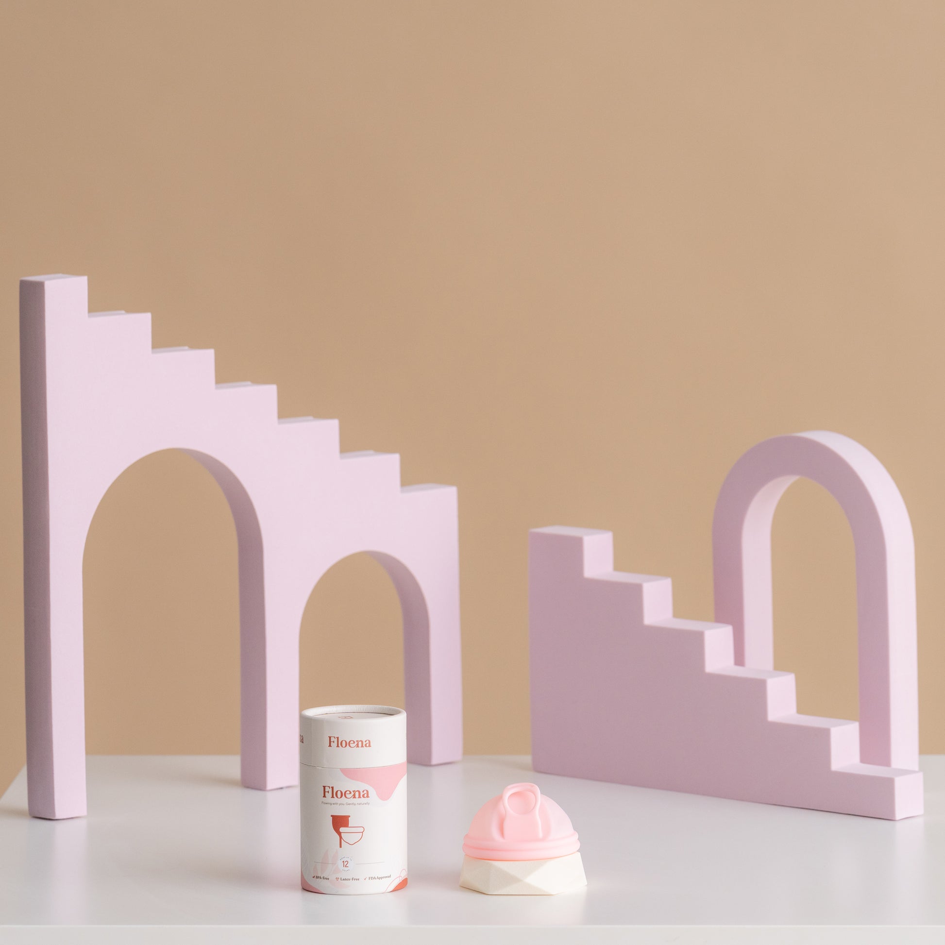 Floena Menstrual Disc in pink silicone beside packaging, set against playful purple geometric blocks. 12-hour leakproof protection for comfort during periods.