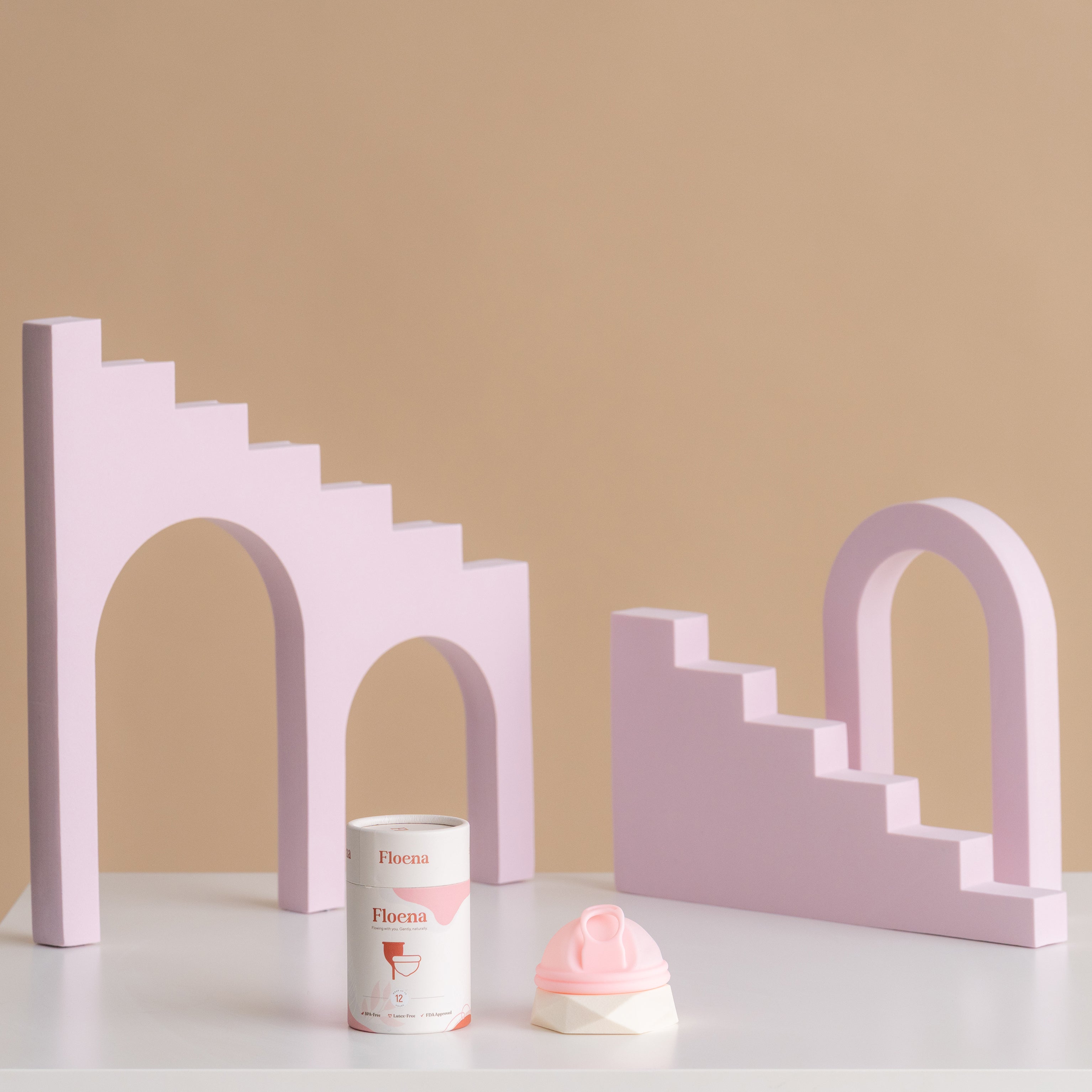 Floena Menstrual Disc in pink silicone beside packaging, set against playful purple geometric blocks. 12-hour leakproof protection for comfort during periods.