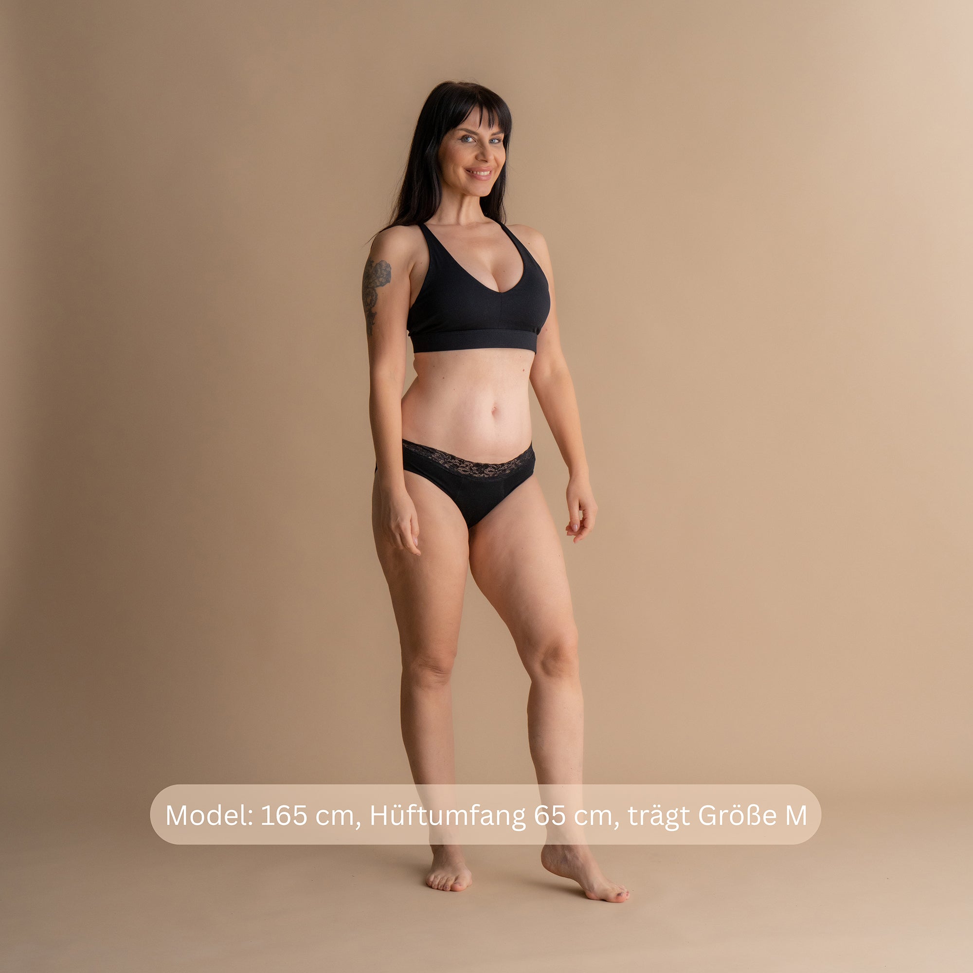 Model 165 cm groß, Hüftumfang 65 cm, trägt Größe M Leakproof Comfort Brief Periodenslip in Schwarz vor beigefarbenem Hintergrund mit Größenhinweis