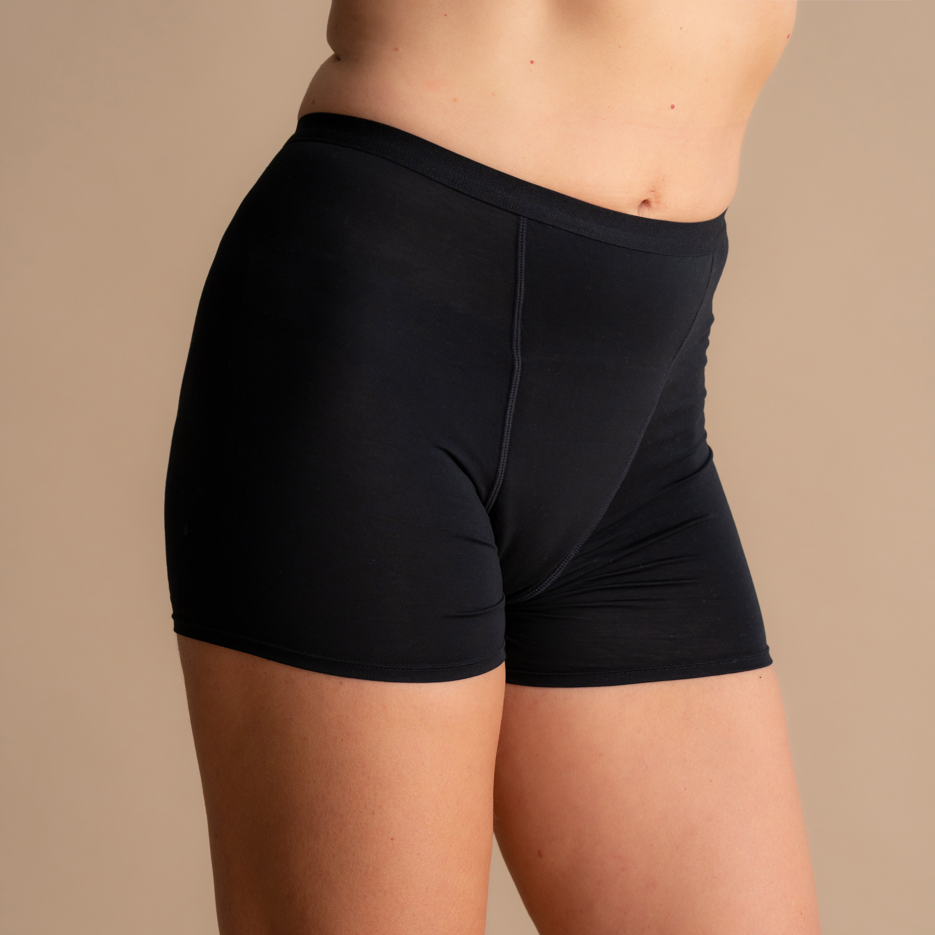 Nahaufnahme der Vorderansicht der schwarzen Leakproof Bamboo Sleep Short Periodenschlafshorts am Model vor beigem Hintergrund.