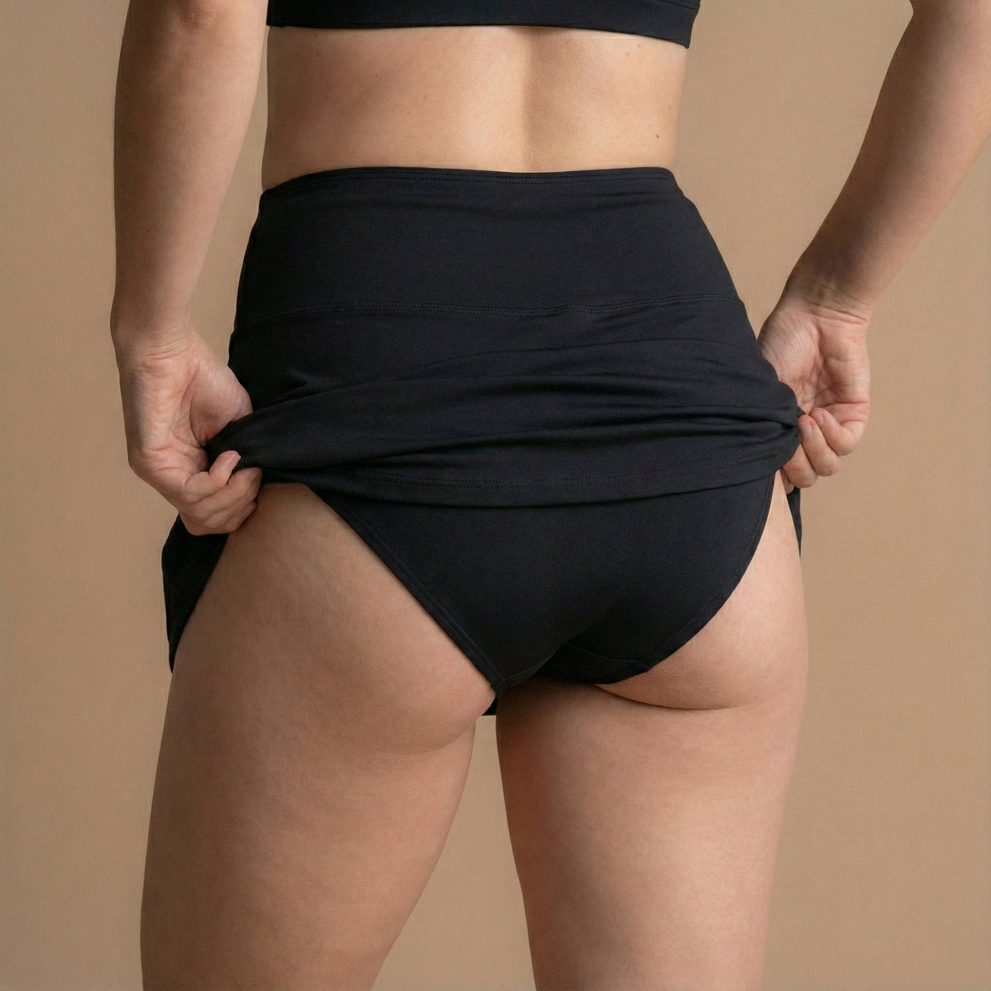 Rear view of a model adjusting the Leakproof Period Swim Skirt, showcasing its discreet, built-in protection. The design offers full coverage with a flattering, high-waisted fit and water-repellent fabric to lock leaks in.