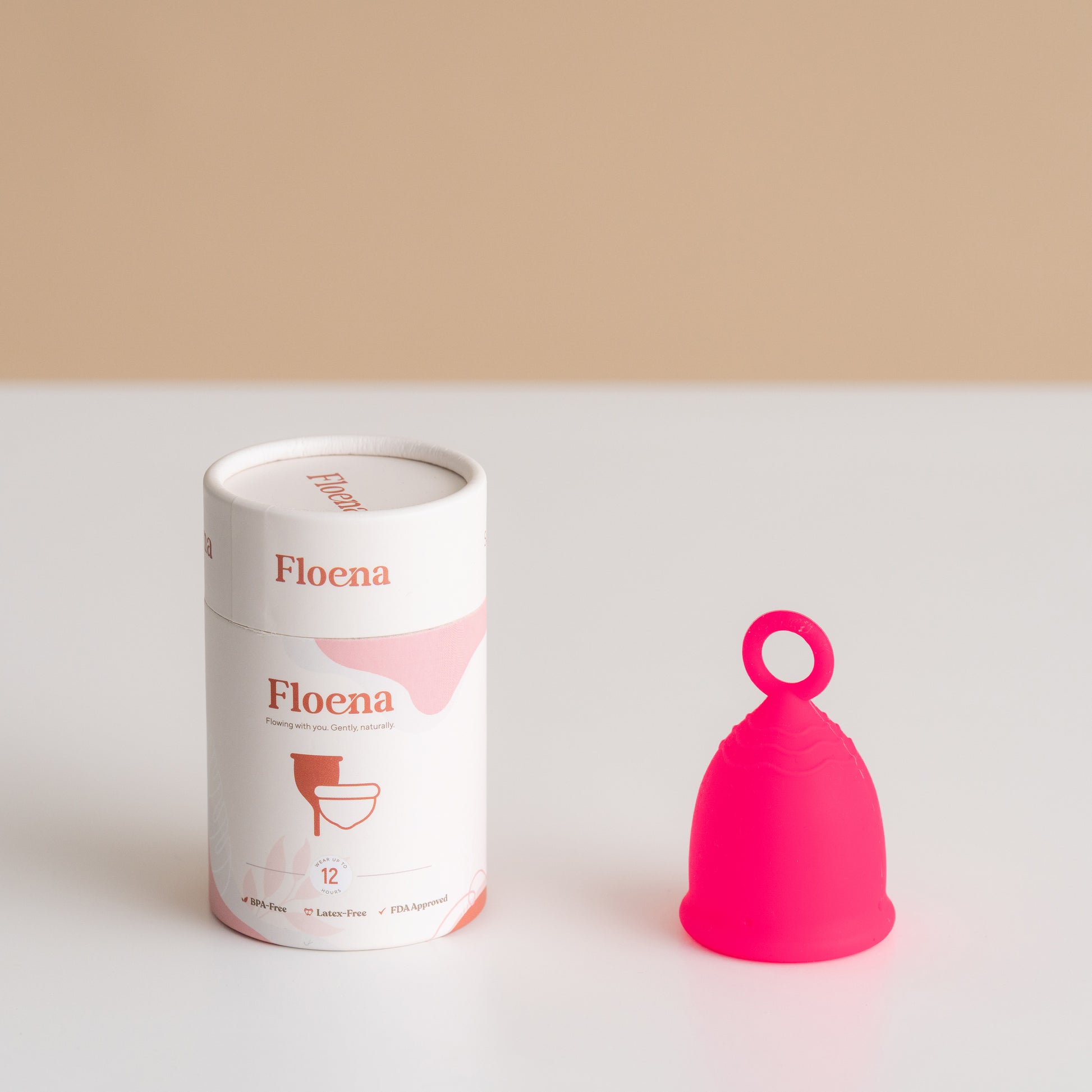 Der pinke Floena Ring-Menstruationscup steht neben seiner Verpackung. Der Cup hat einen komfortablen, ergonomischen Ring für eine einfache Handhabung und bietet bis zu 12 Stunden auslaufsicheren Schutz.
