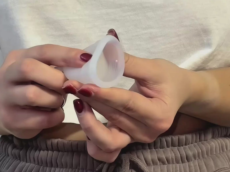 Hände zeigen die U-Falttechnik zum Einführen einer Menstruationstasse oder eines Menstruationsdisks, mit Schritt-für-Schritt-Faltmethode.